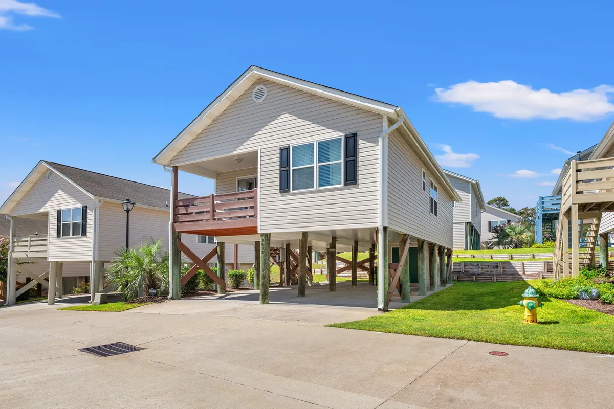 A cheerful exterior view of the raised, stand-alone home surrounded by lush greenery, featuring a concrete driveway and a welcoming porch. The scene hints at the vibrant atmosphere perfect for outdoor gatherings, morning coffee, or relaxing at sunset.