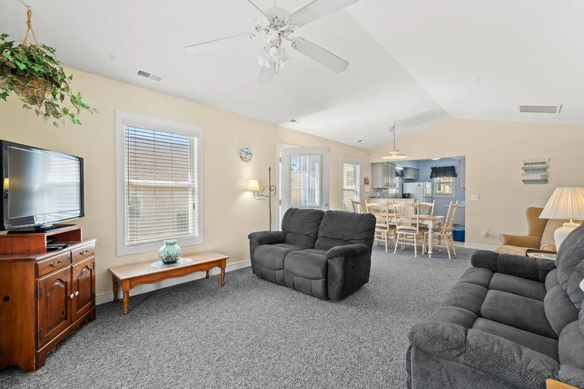 A spacious open-plan living and dining area with a comfortable sofa set facing a TV stand, coffee table, and the dining area visible beyond. Natural light floods the space, creating a cheerful and inviting atmosphere perfect for relaxation or social gatherings.