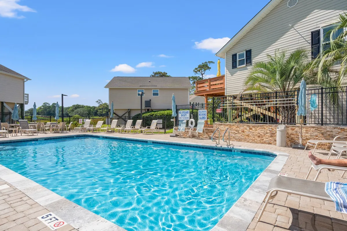 The image showcases the inviting outdoor pool surrounded by comfortable lounge chairs and lush greenery, creating a private oasis for guests. The setup hints at leisurely afternoons spent swimming, sunbathing, or relaxing with friends and family in a serene setting just minutes from the beach.
