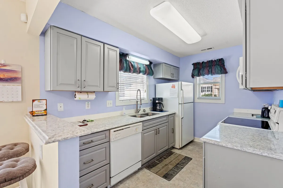 A bright, open kitchen with gray cabinetry, polished granite countertops, and ample natural light streaming in through a window. Modern appliances and a welcoming atmosphere make this kitchen ideal for cooking, gathering, and sharing memorable meals.