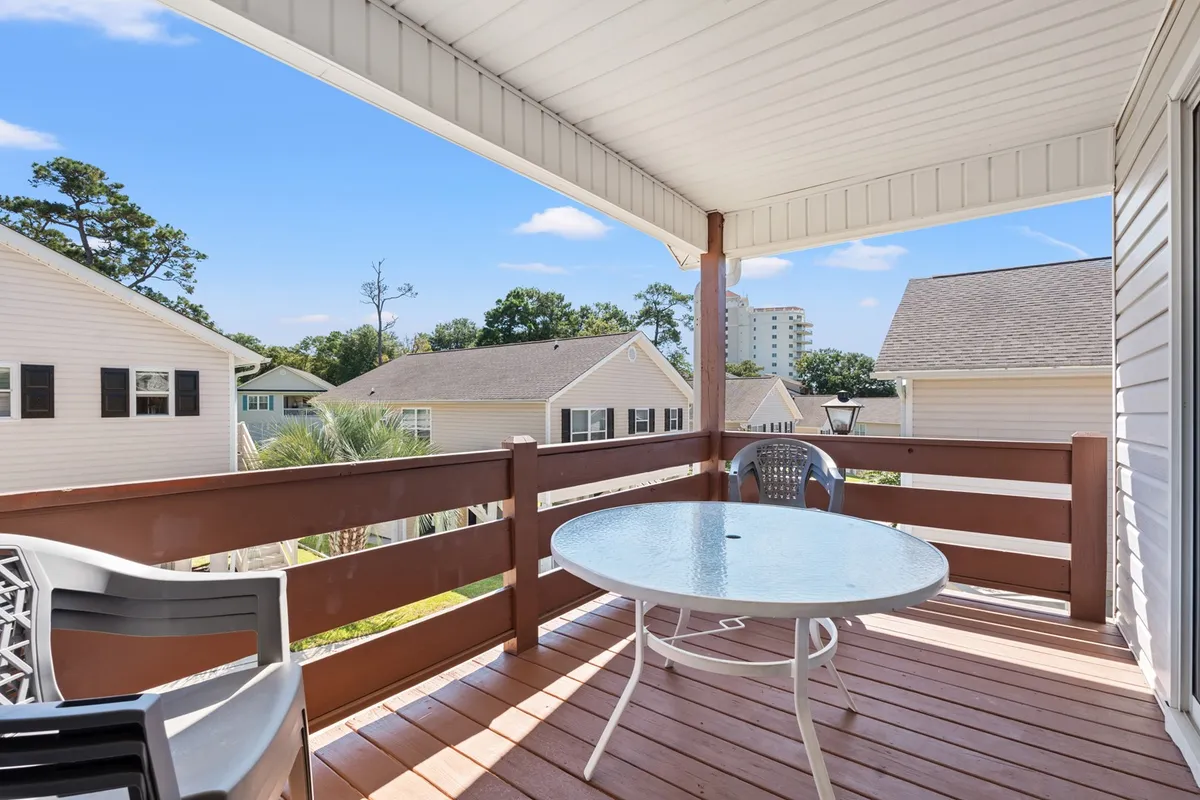 A private outdoor balcony space furnished with a glass-top table and chairs, bordered by sturdy railings. The setting is perfect for enjoying morning coffee, relaxing, or dining while taking in fresh air and outdoor views.