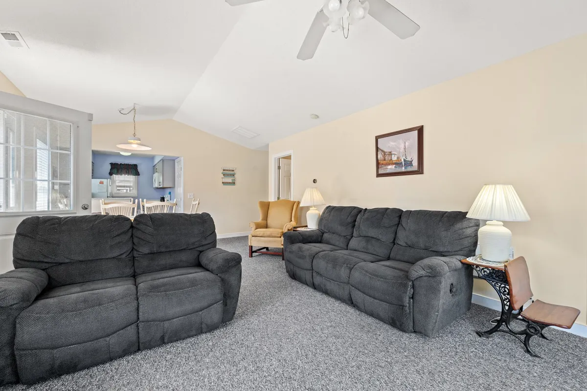 A wide, welcoming living room featuring two cozy sofas, soft lighting from elegant lamps, artwork on the walls, and a dining area visible in the background. The space is inviting for relaxing, socializing, or entertaining guests, with a comfortable ambiance that encourages guests to unwind and enjoy special moments together.