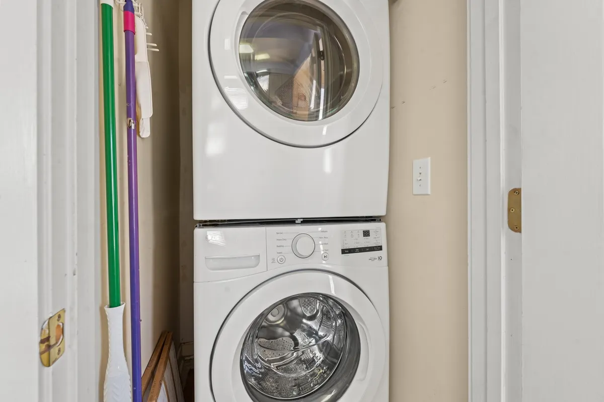 A practical laundry nook with a stacked washer and dryer, laundry supplies, and an open doorway, illustrating the convenience and accessibility of this amenity within the living space.